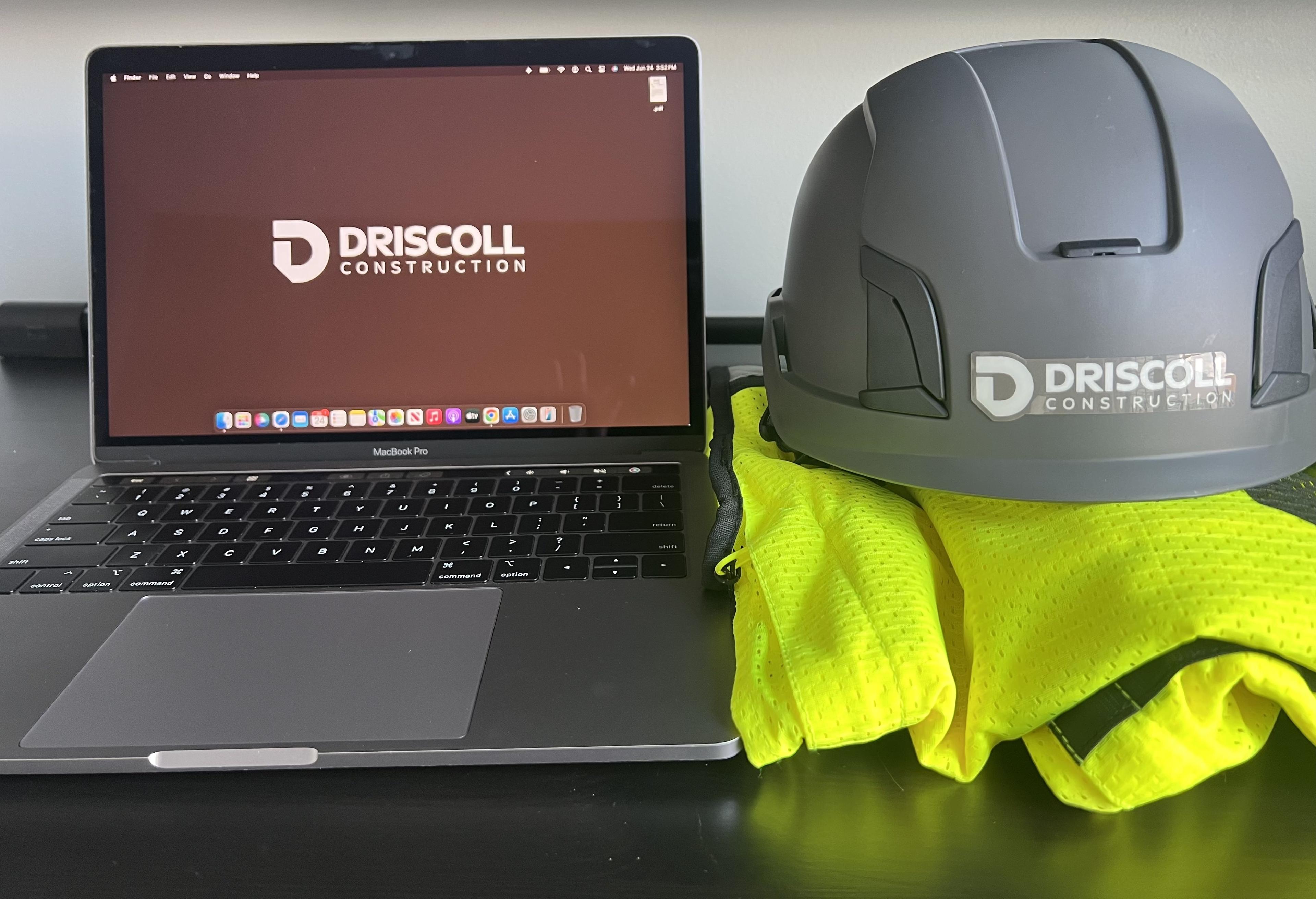 Driscoll Construction branded helmet beside a laptop