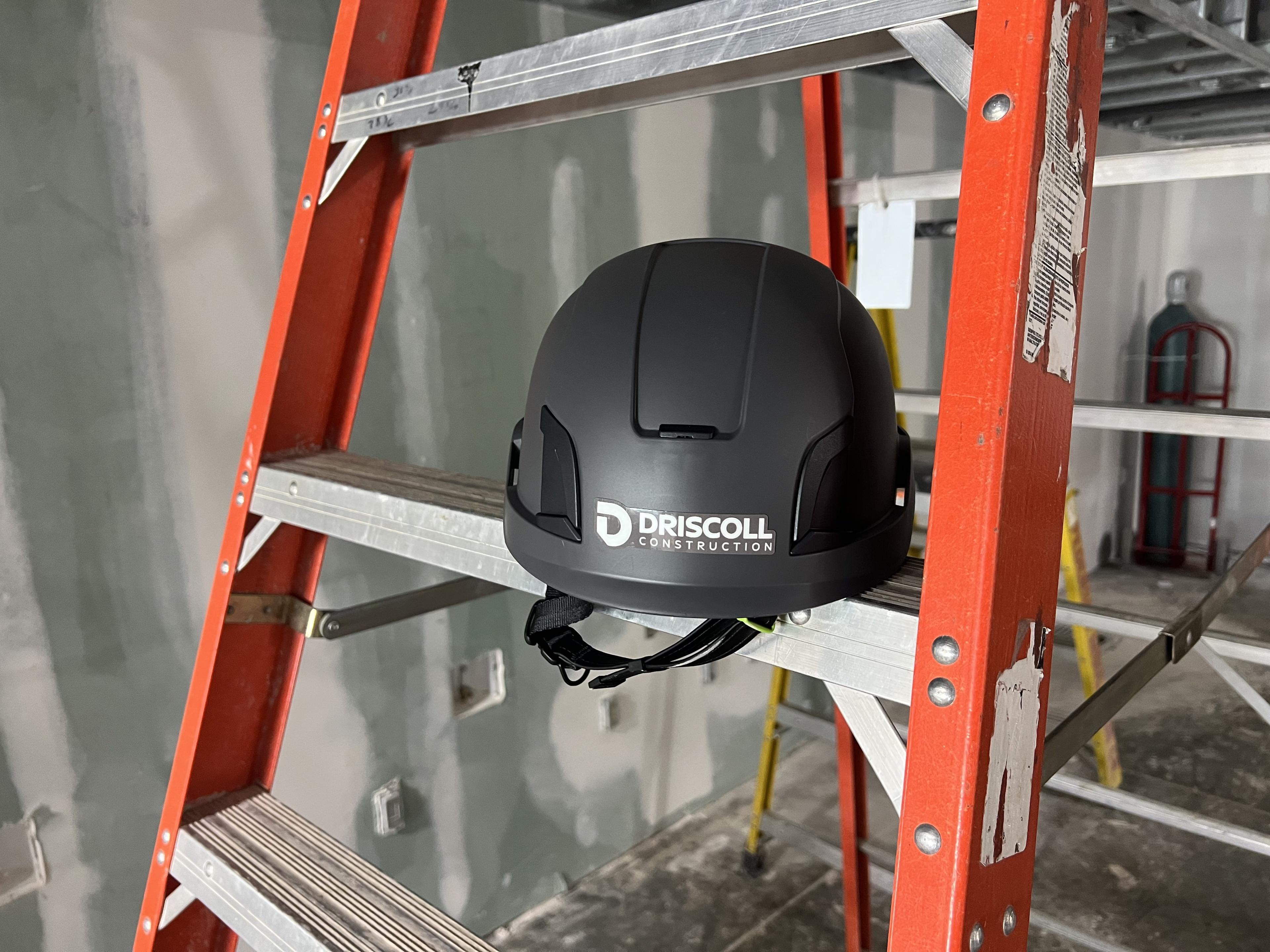 Driscoll Construction branded helmet set among ladders on an active jobsite